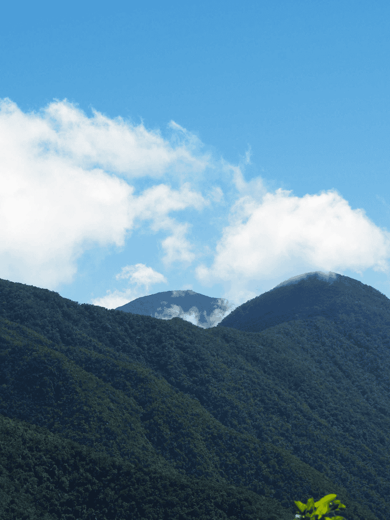 Lush green mountains under blue sky with white clouds, scenic nature landscape.