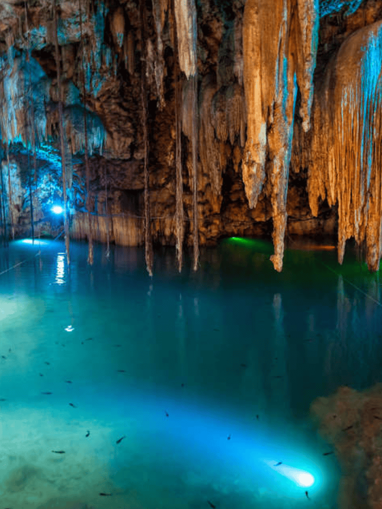 Stalactites and underground river in a stunning cave with colorful lighting.