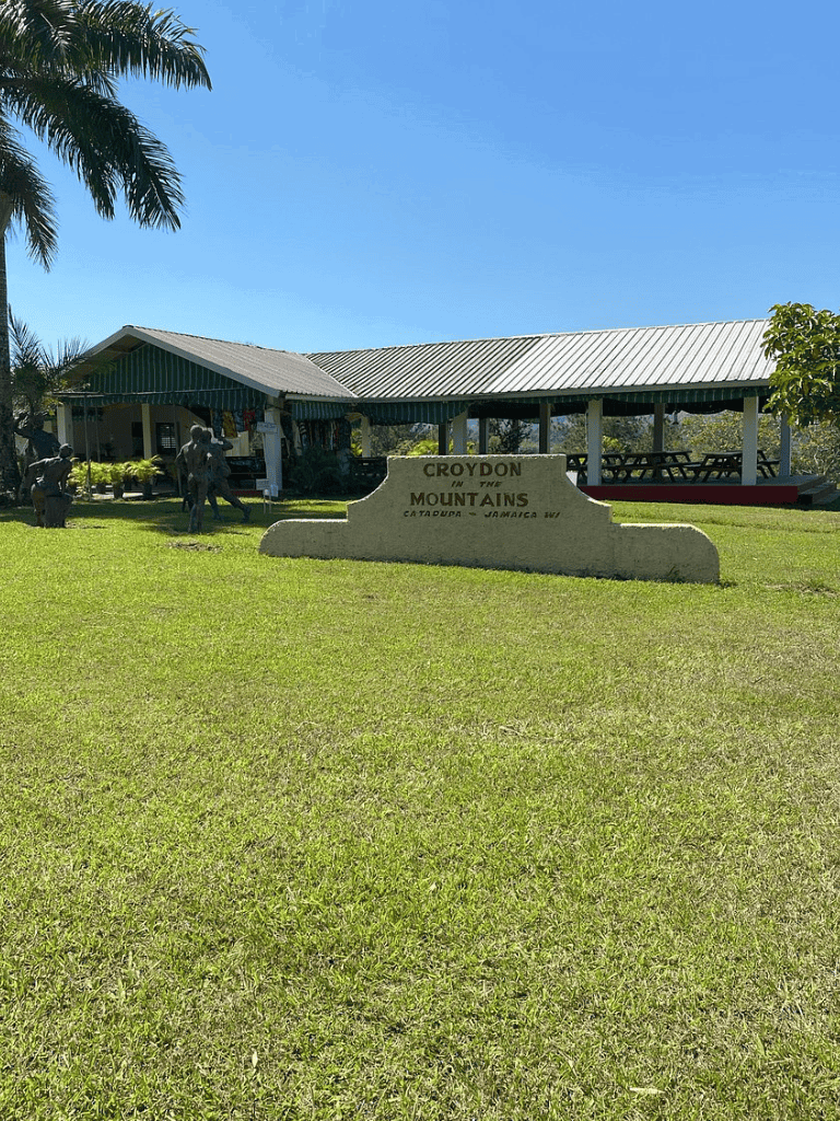 Croydon in the Mountains sign at Catadupa Jamaica, lush green park with tourist attraction and outdoor seating area.