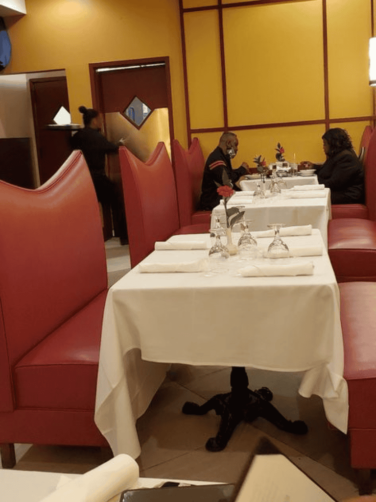 Elegant restaurant interior with red booths, white tablecloths, and two guests dining, set amid warm yellow walls.