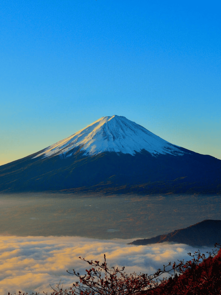 Majestic Mount Fuji with snow-capped peak, sunrise sky, and surrounding clouds in Japan.
