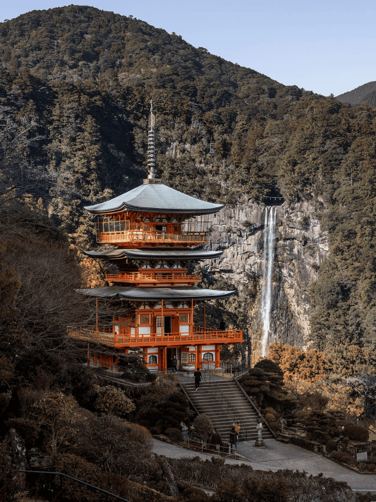 Stunning Japanese pagoda with waterfall and mountain scenery in the background.