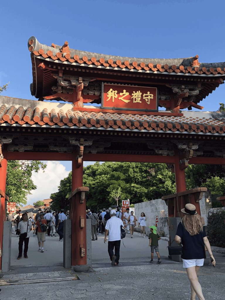 Traditional Japanese temple entrance with tourists and lush greenery in background.