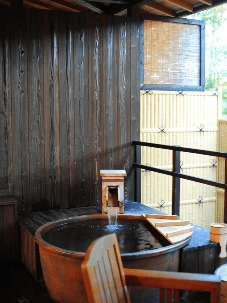Relaxing outdoor hot spring bath with bamboo fencing and wooden decor.