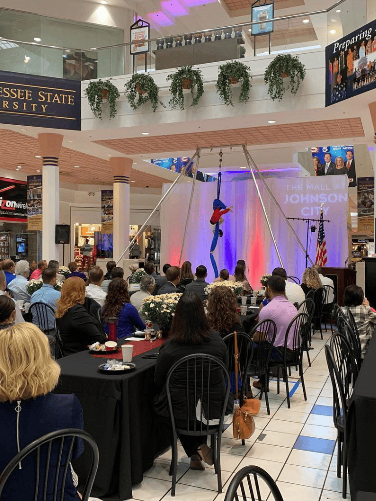 Aerialist performing at QuestForDirections event in a mall auditorium with audience and Tennessee State University banners.