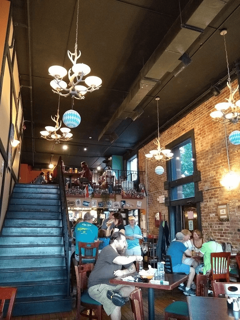 Cozy restaurant interior with exposed brick walls, modern chandeliers, and customers dining and socializing.