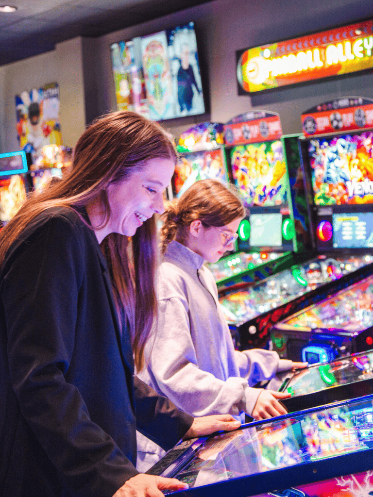 Playing pinball at arcade with friends, colorful arcade games, entertainment, fun, QuestForDirections.