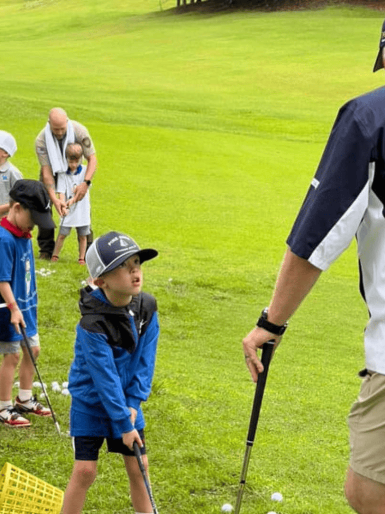 Kids learning golf with coach on lush green golf course.