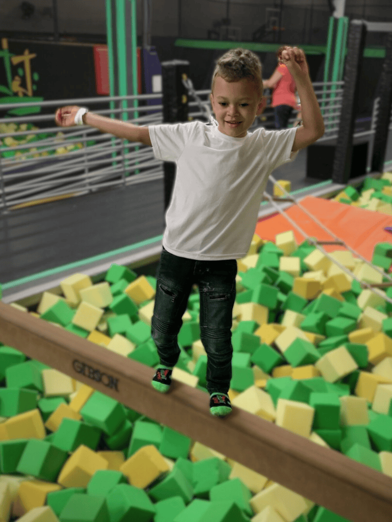 1. Child balancing on a wooden beam over foam blocks at indoor playground.
