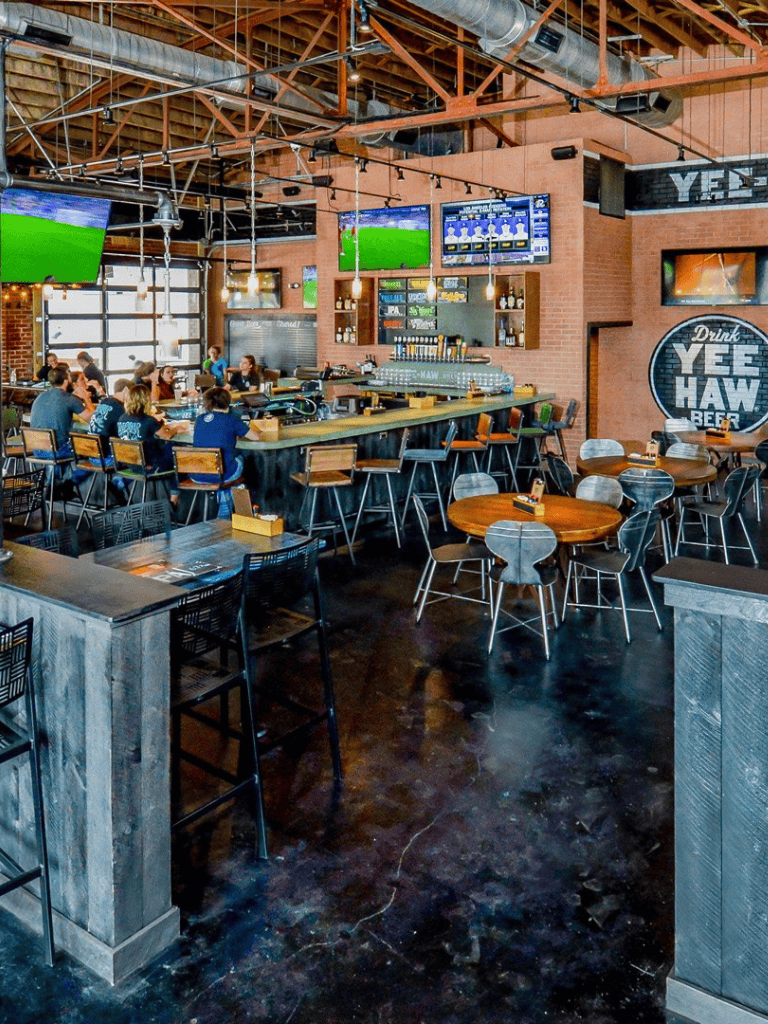 Modern sports bar interior with multiple TV screens, communal seating, and a lively atmosphere for sports fans.