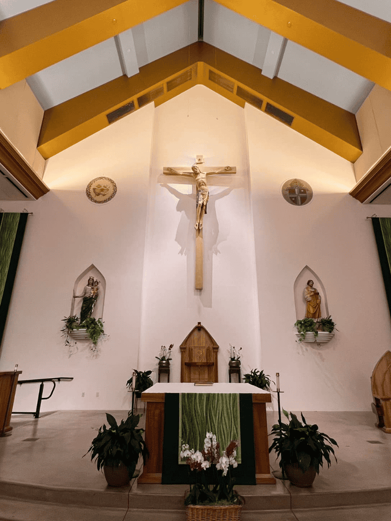 Elevated church altar with crucifix, statues, and religious symbols in a contemporary chapel setting.