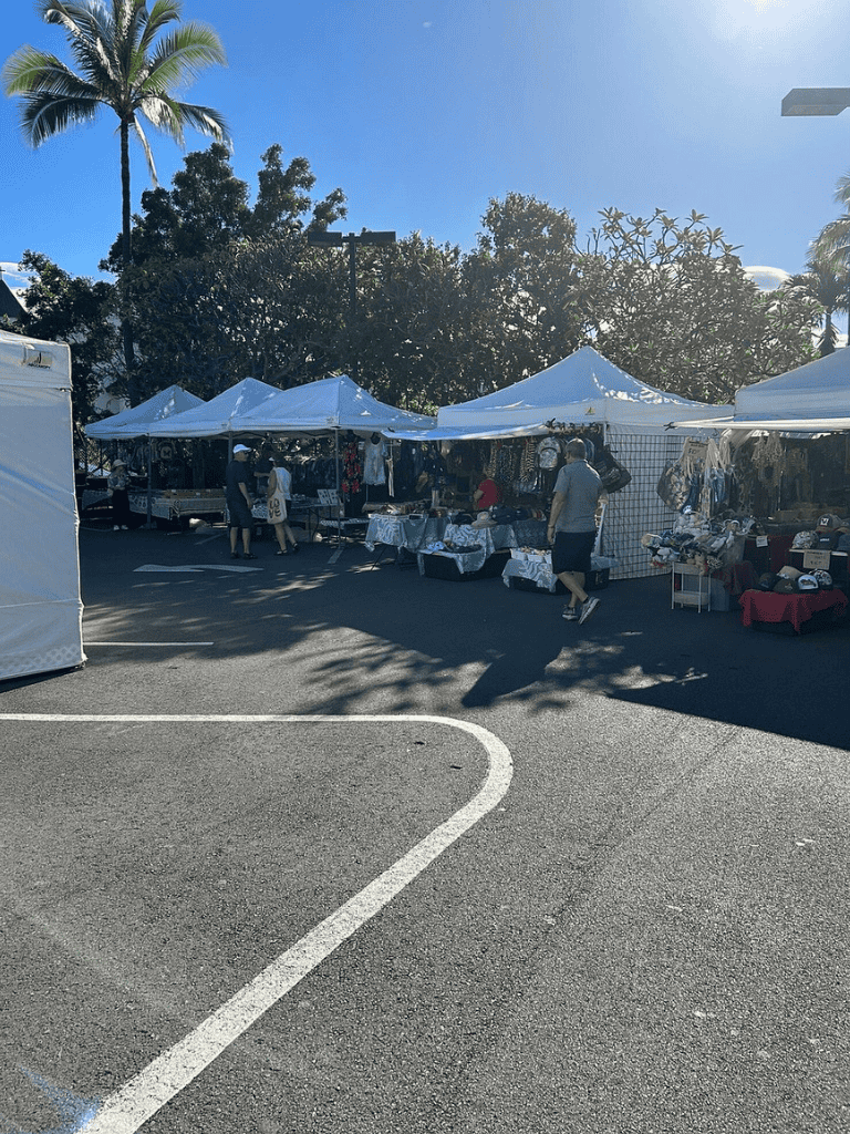 Colorful outdoor market with white tents, vendors selling accessories, and shoppers under sunny skies.