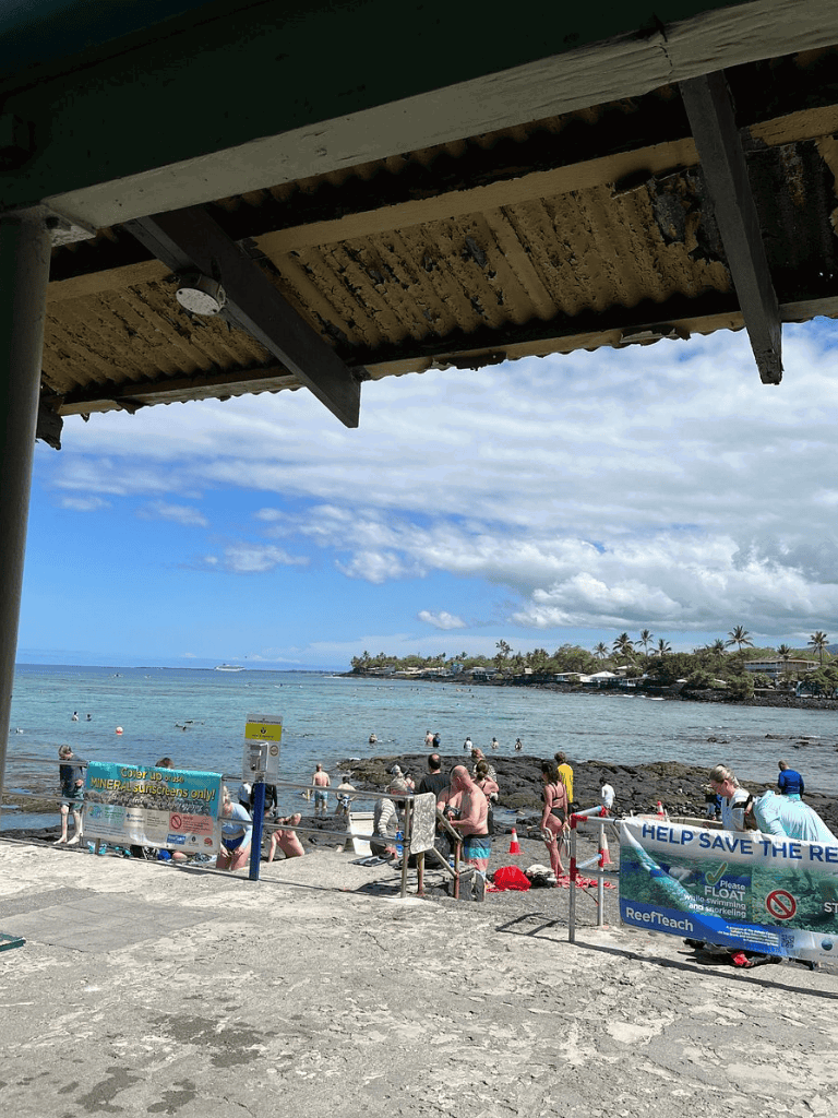 Bright sunny beach scene viewed from under an overhang at QuestForDirections. Swimmers enjoy the clear water and scenic coastline.