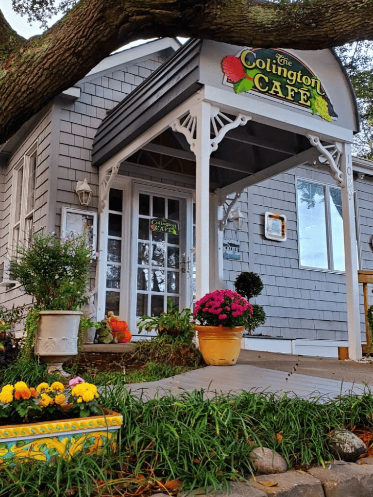 Charming house entrance with colorful flowers and a "Colington Café" sign, inviting and cozy.