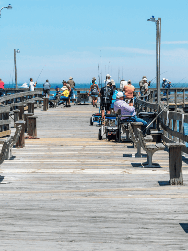 Accessible fishing pier with people enjoying fishing and ocean views, featuring seating and railings.