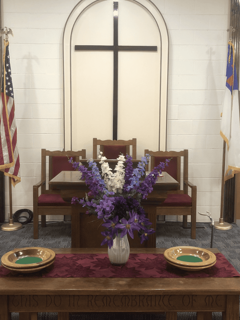 Altar with cross and flower arrangement, church interior for worship or religious events.