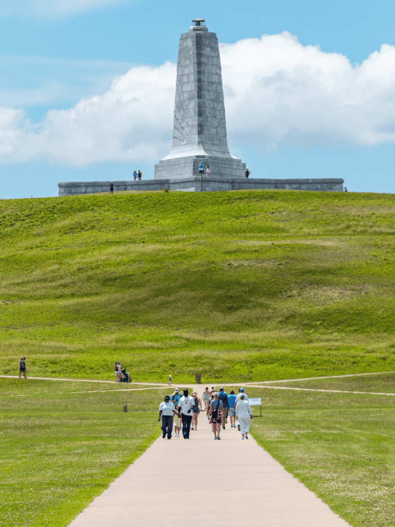 Historic monument on grassy hilltop with visitors and clear sky.