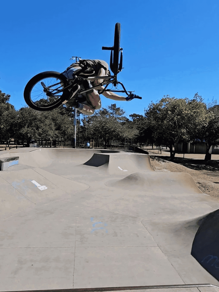 BMX bike trick at skate park with clear blue sky in the background.