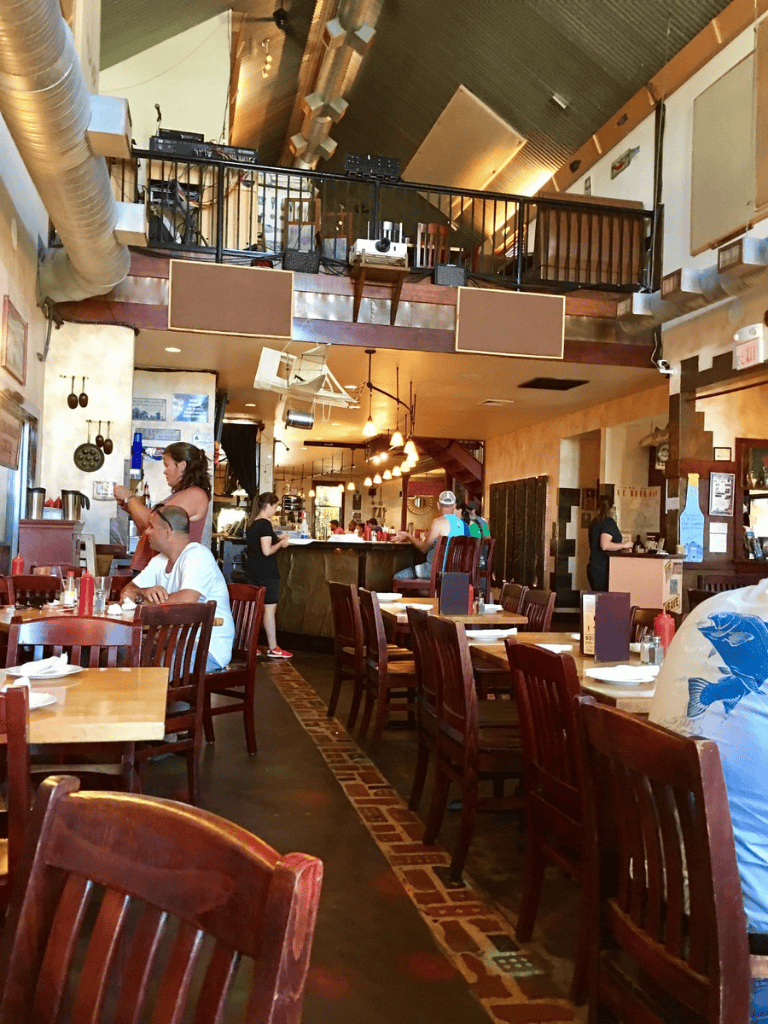 Cozy restaurant interior with wooden furniture, upper balcony, and warm lighting, ideal for dining and socializing.