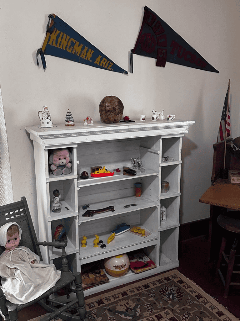Vintage white wooden shelf with toys and decorations, surrounded by flags and antique items.