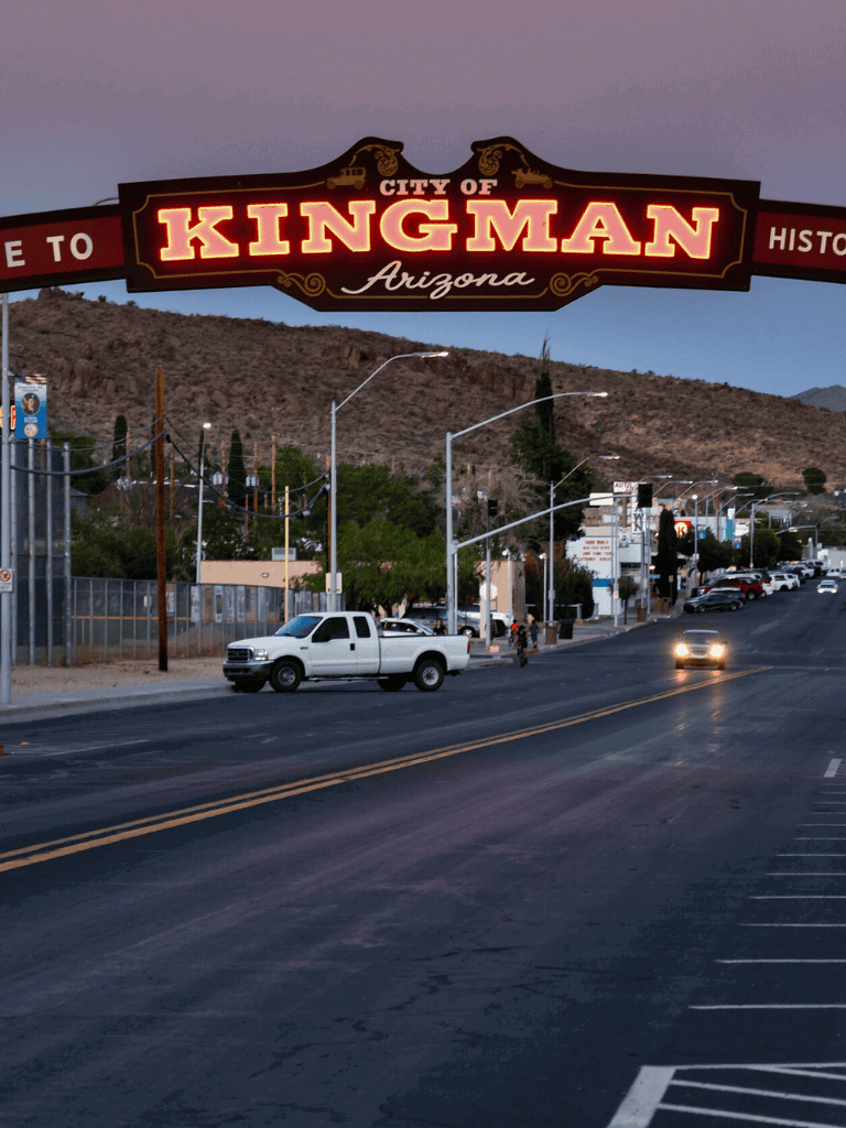 Historic Kingman Arizona city sign at dusk with cars and mountains in the background.
