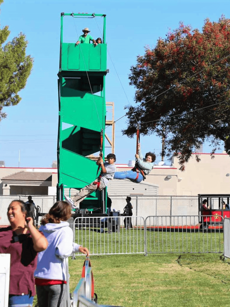 Rope swing ride at outdoor event with children, trees, and a fun fair atmosphere.