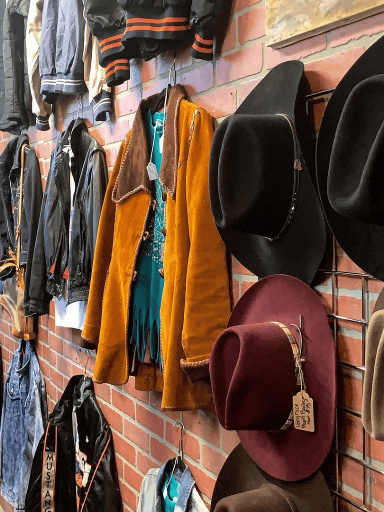 Second-hand vintage clothing store, leather jackets, fur coats, wide-brimmed hats, brick wall display, fashion accessories, unique style, thrift shopping.