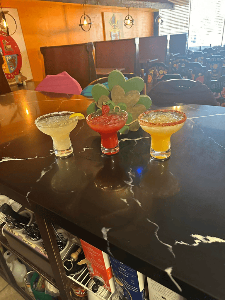 Colorful margaritas on a black marble table at a lively Mexican restaurant, perfect for family gatherings and celebrations.