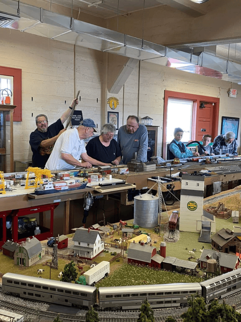Miniature train display at QuestForDirections hobby event, showcasing detailed model scenery and enthusiastic hobbyists.
