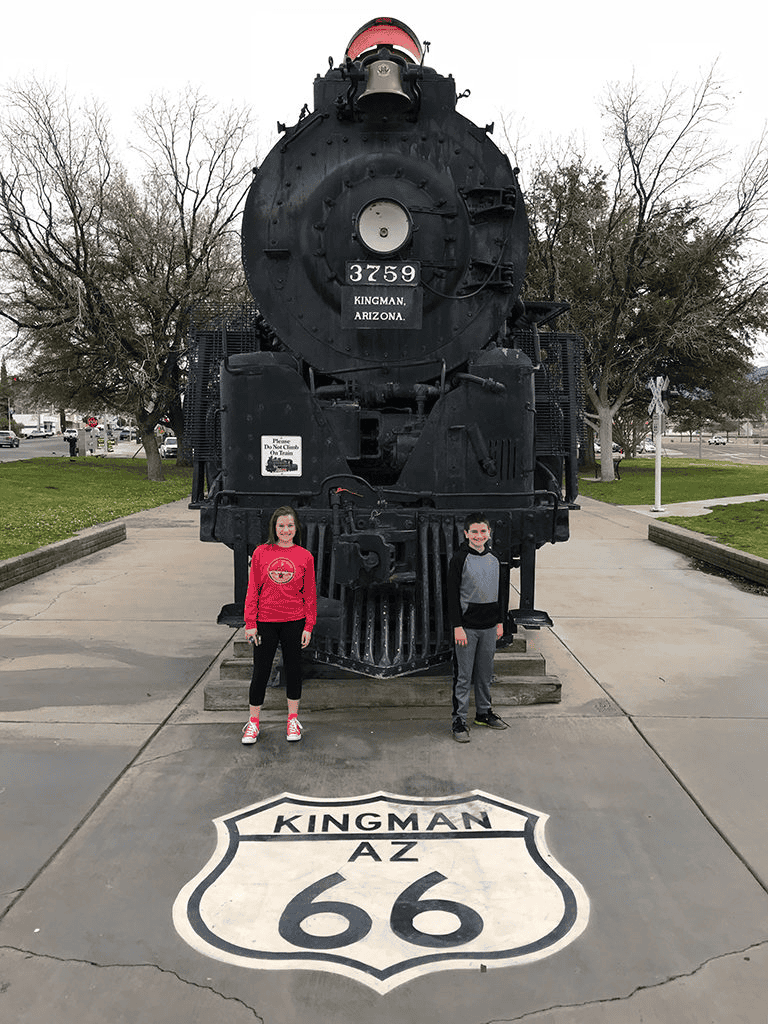 Vintage steam locomotive Kingman AZ Route 66 monument scene with two kids standing beside it.