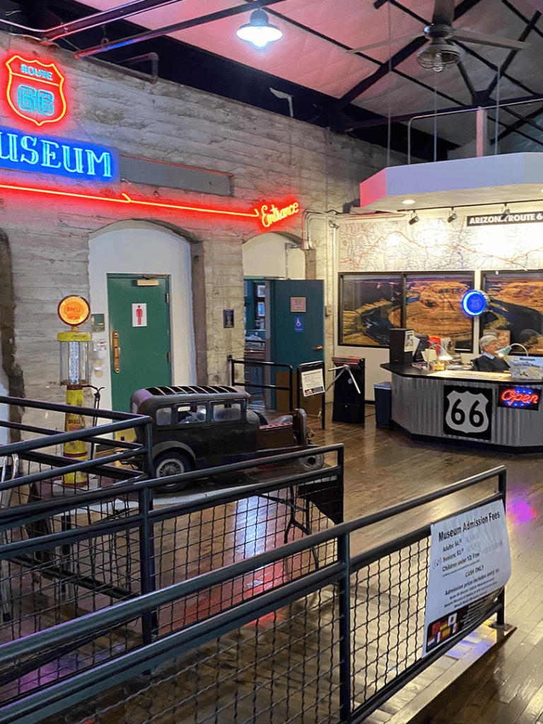 Route 66 neon museum sign with vintage car exhibit inside a museum.