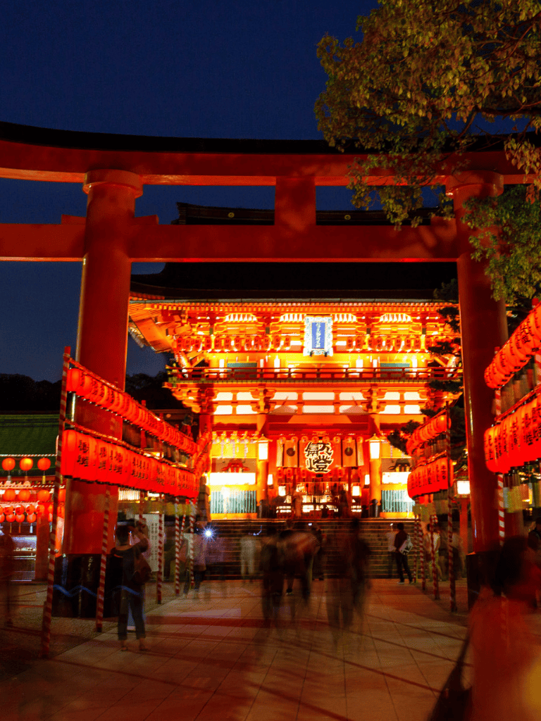 Vibrant illuminated Japanese shrine gate with visitors at night, cultural landmark, and traditional architecture.