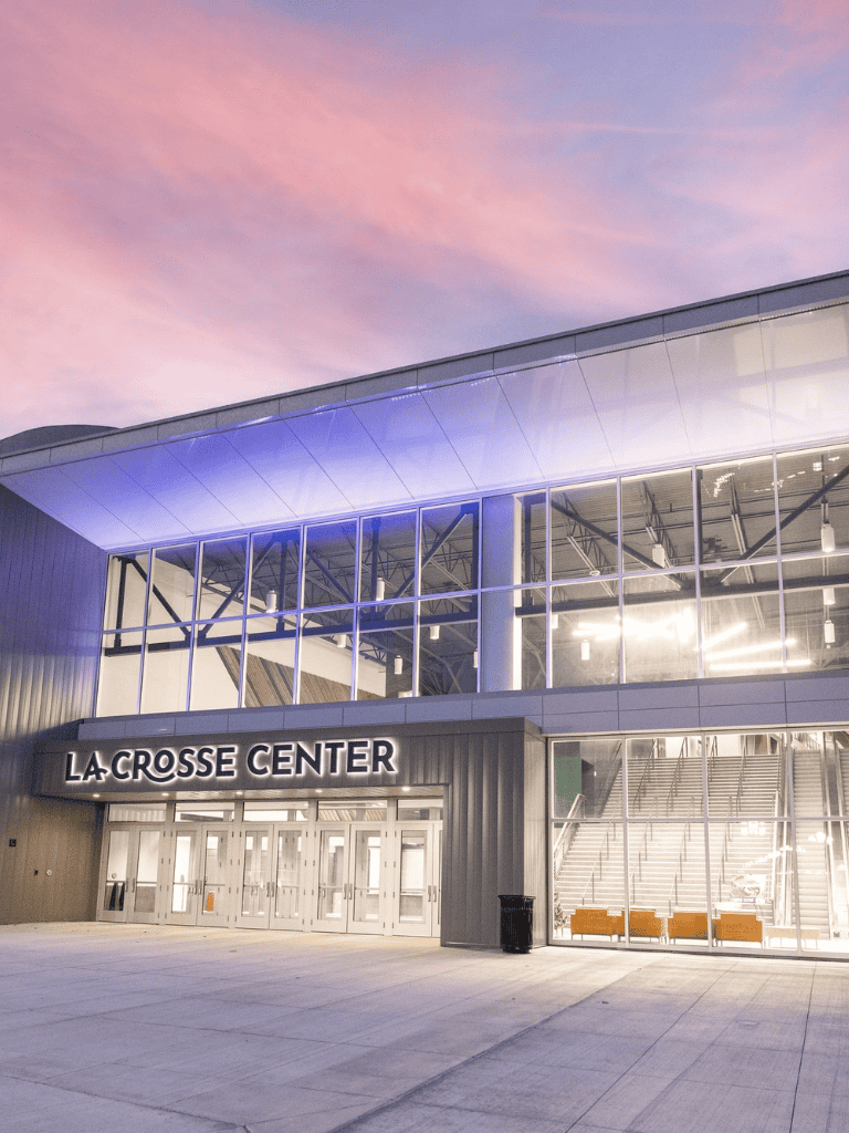Modern La Crosse Center exterior at dusk with illuminated signage and large glass windows, a prominent event venue in La Crosse, Wisconsin.