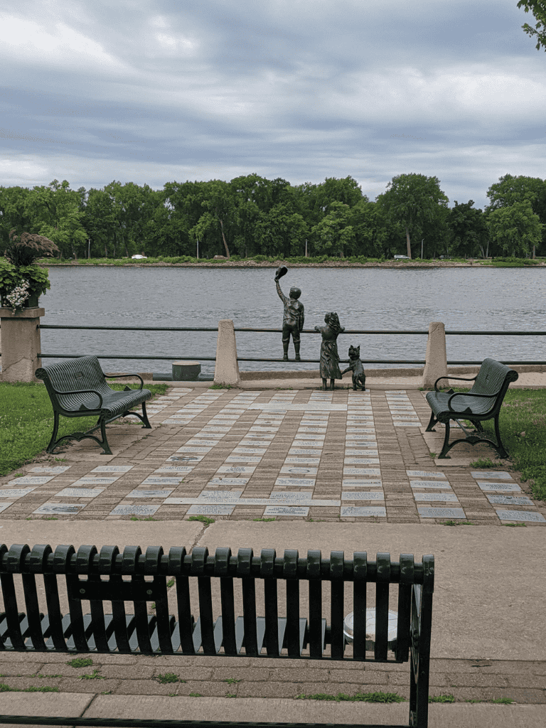 Bronze statue of children at riverside park, surrounded by benches and greenery, perfect for outdoor exploration.