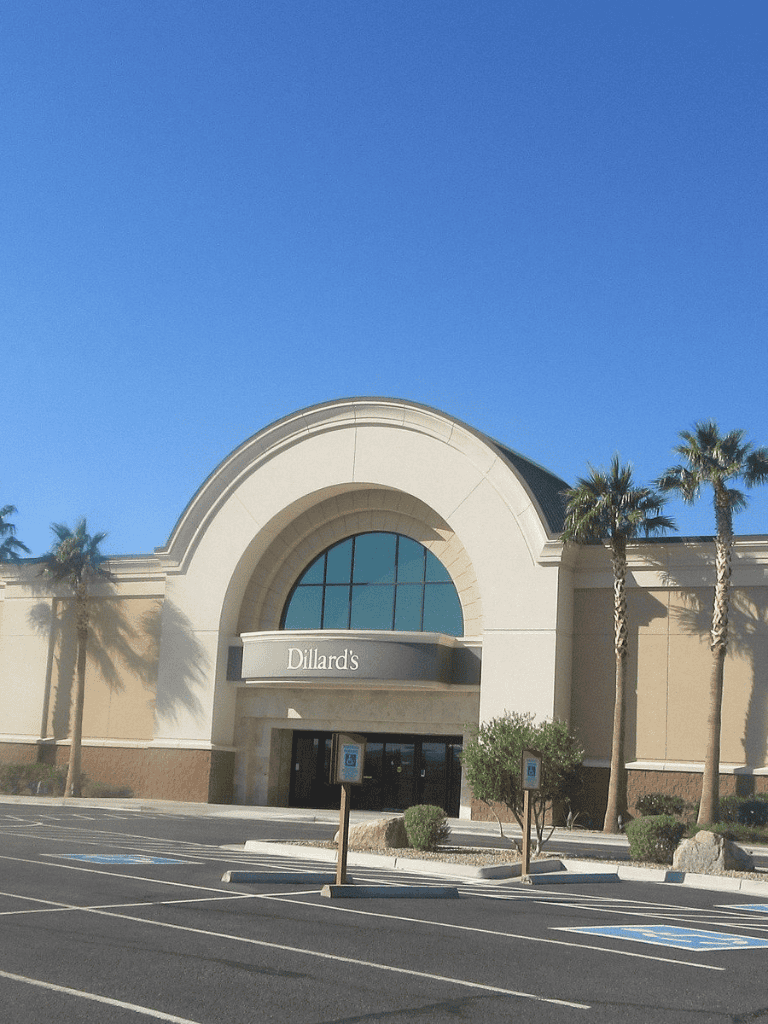 Modern shopping mall entrance with palm trees and clear blue sky.