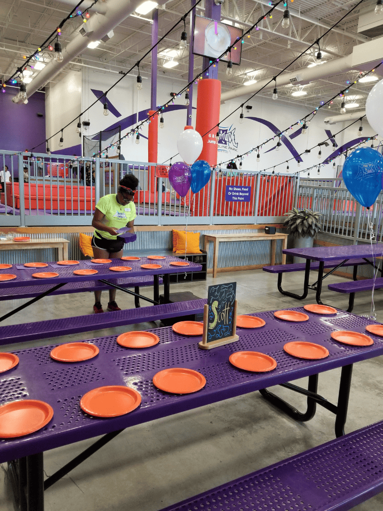 Enjoying a fun indoor birthday party at Quest for Directions trampoline park, featuring colorful balloons, purple tables, and orange plates for kids.