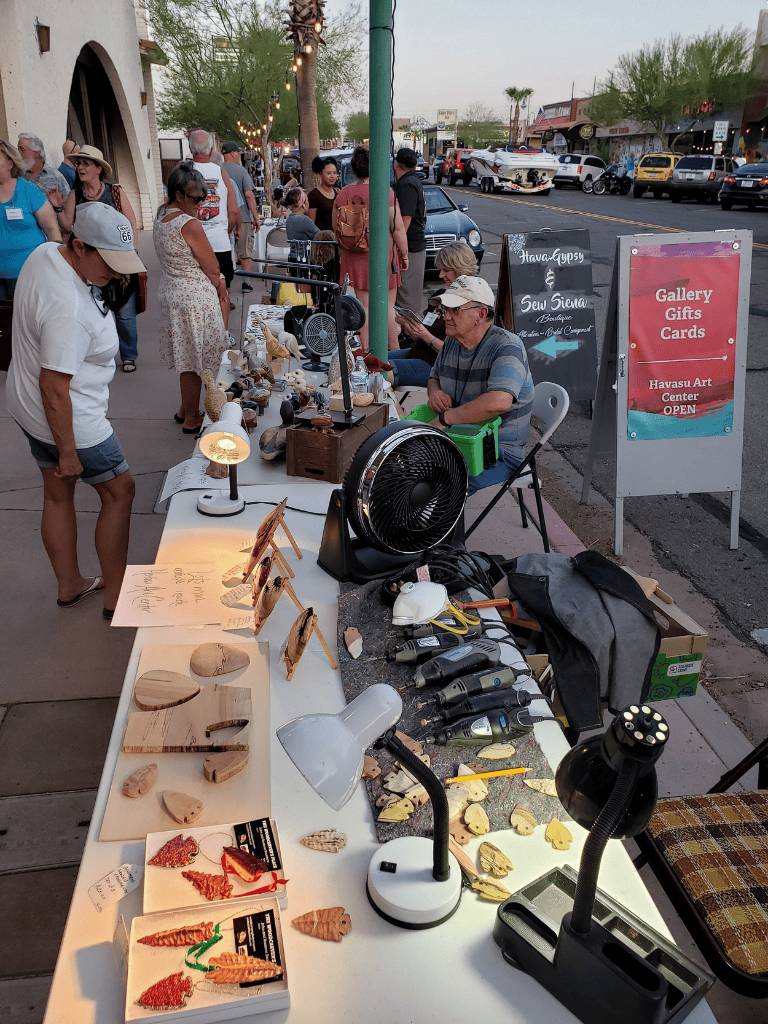 Colorful outdoor arts and crafts market at sunset with vendors and shoppers on a lively street.