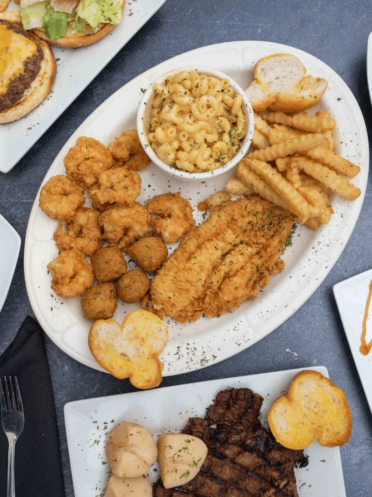 Crispy fried chicken with mac and cheese, crinkle-cut fries, and hush puppies on a white platter.
