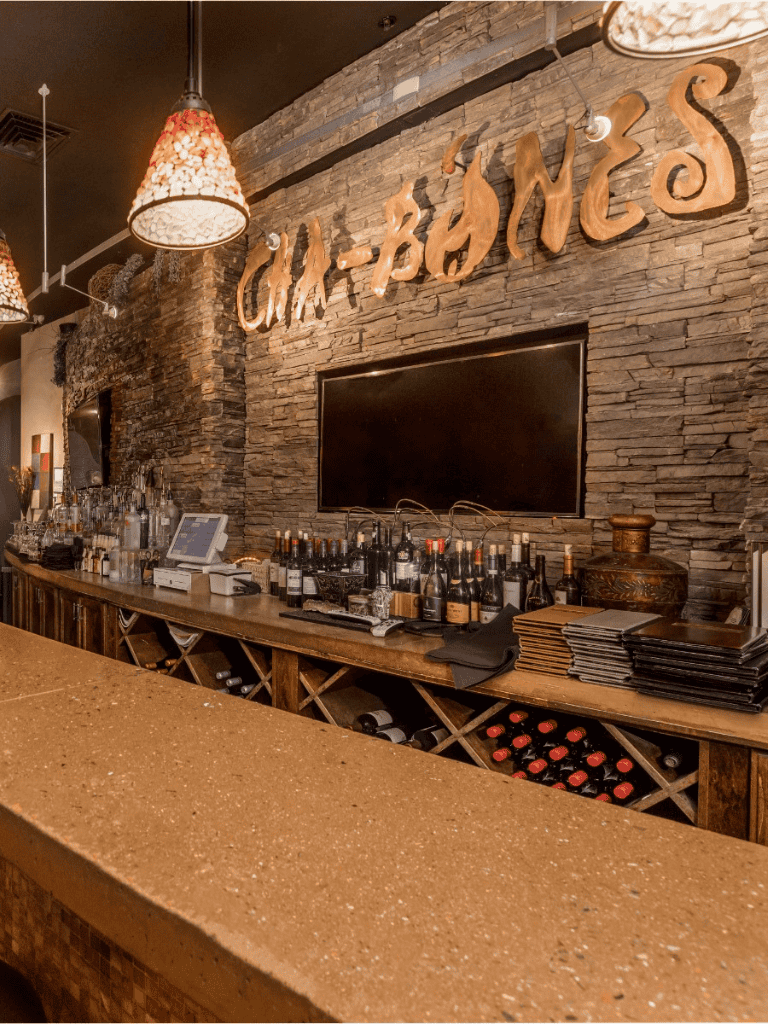 Charming restaurant bar with wine bottles, rustic brick wall, and elegant decor for dining.