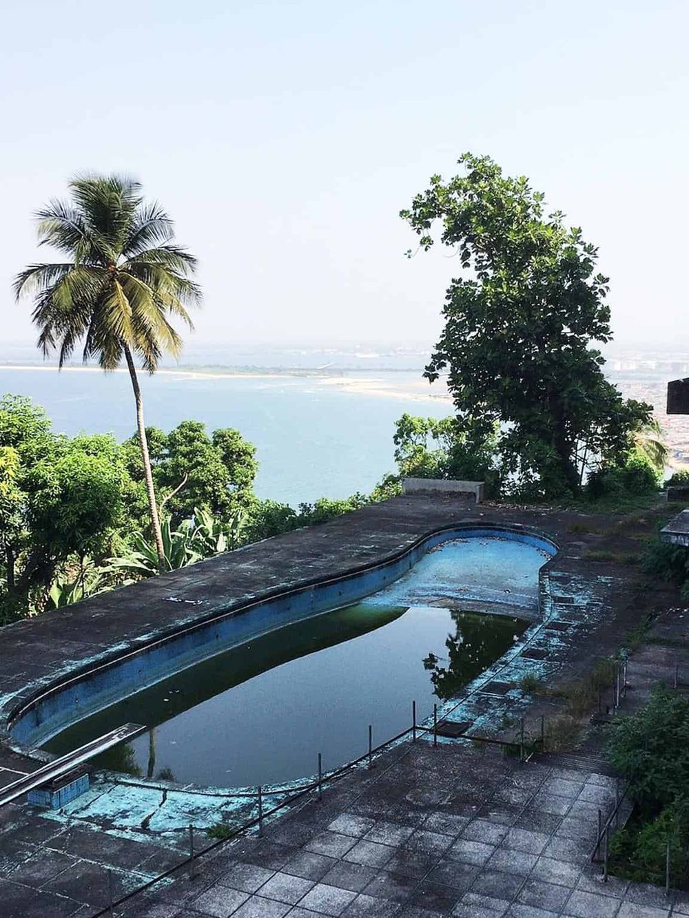 Old swimming pool with water and scenic ocean view in background.