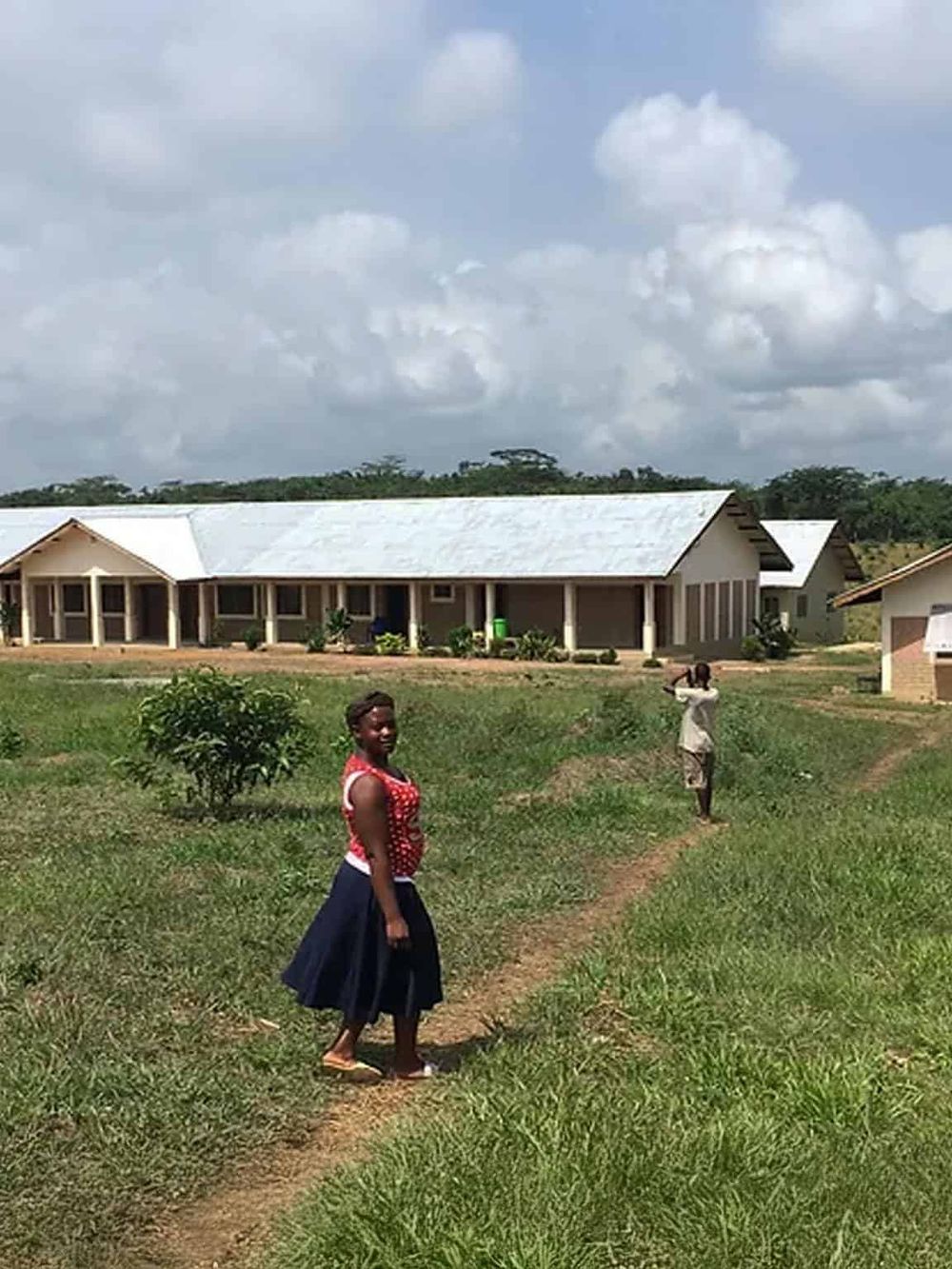 Rustic community housing with people walking pathways, lush green landscape, and a cloudy sky, showcasing rural living and infrastructure.