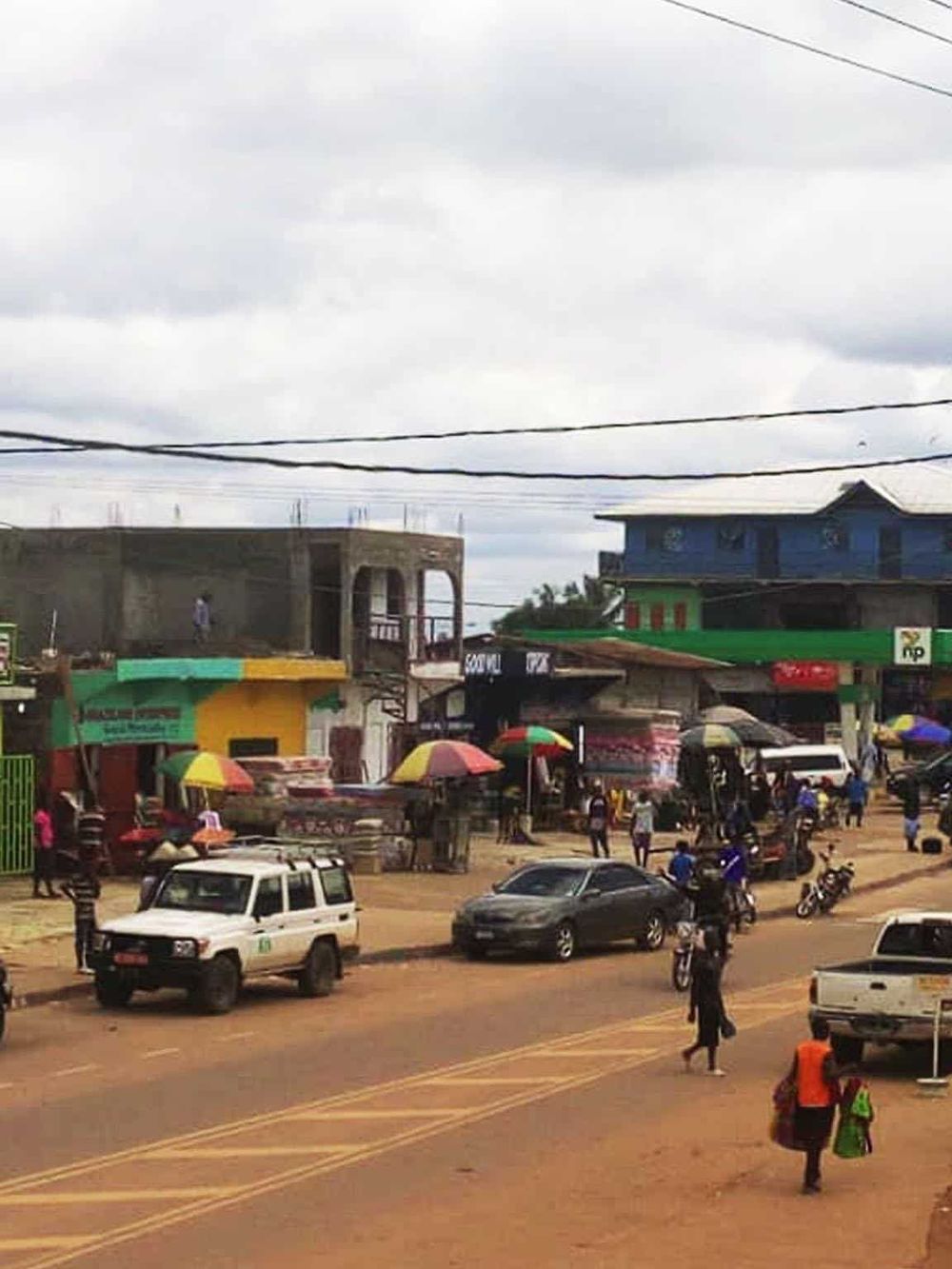 Colorful marketplace with shops, cars, and people on a busy street in QuestForDirections.