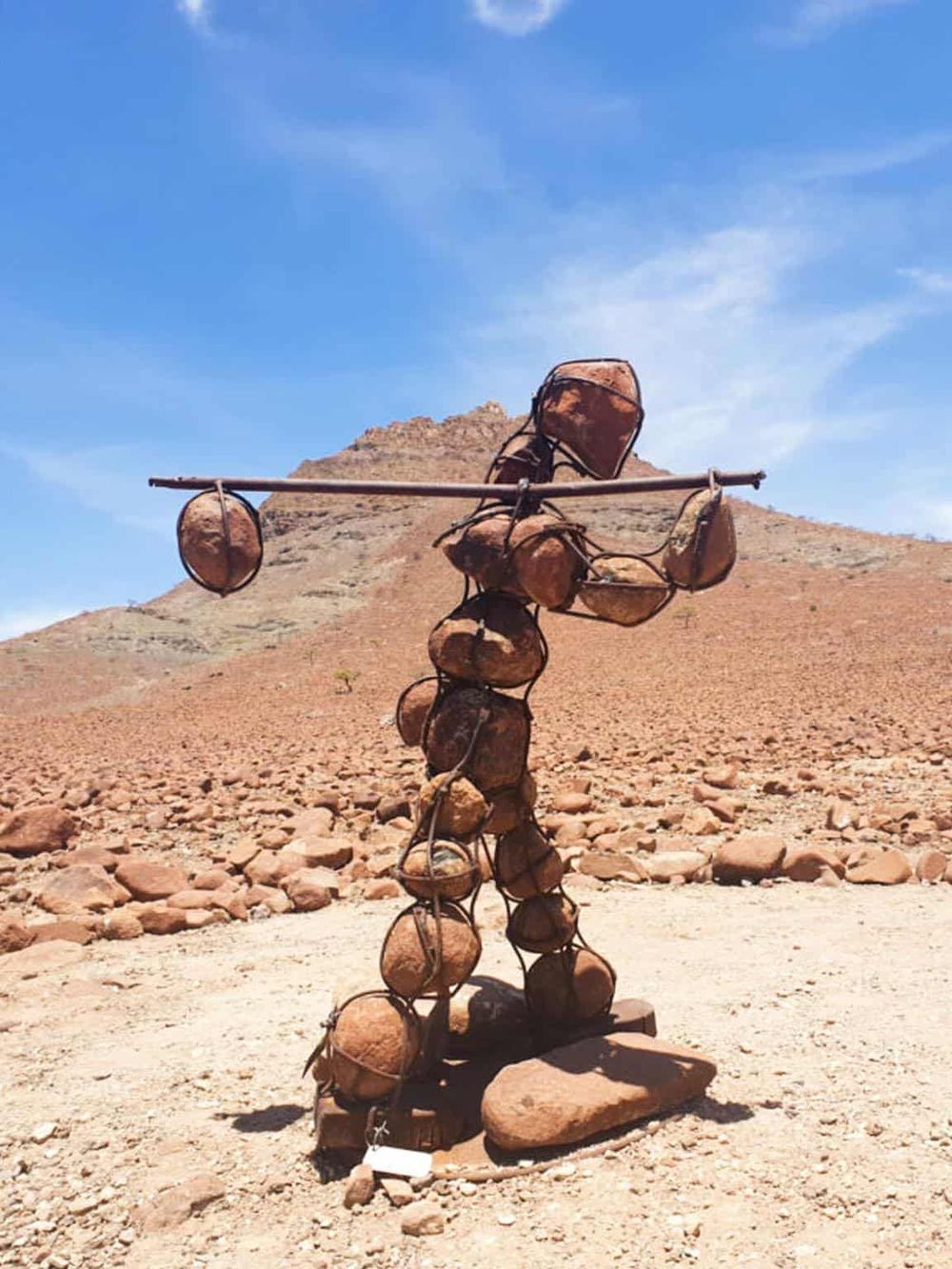 Rustic desert survival sculpture made of rocks against a mountainous landscape and blue sky.