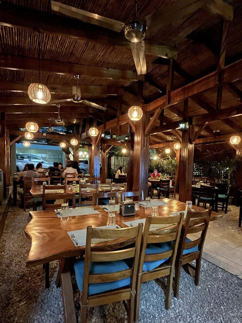 Cozy wooden restaurant interior with warm lighting, outdoor seating, and guests enjoying their meals.