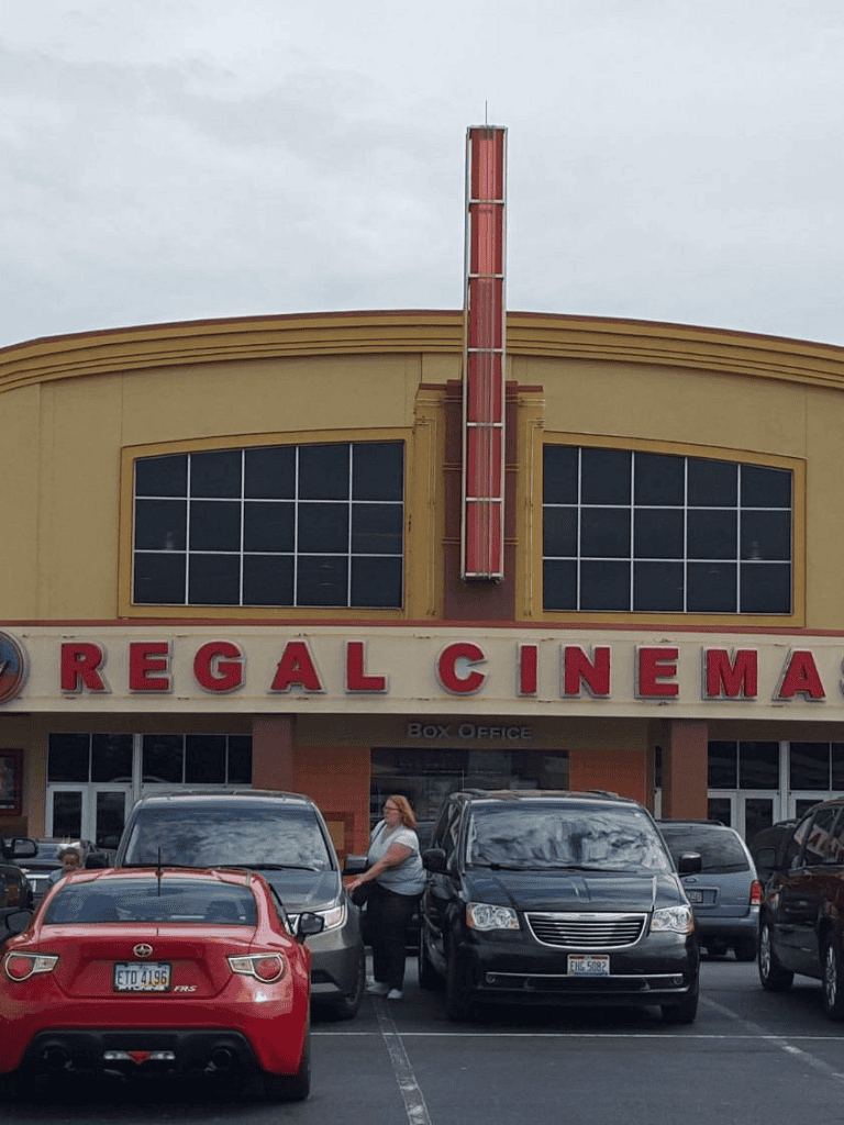 Vintage Regal Cinema building with parking lot and people in front, downtown theater history.