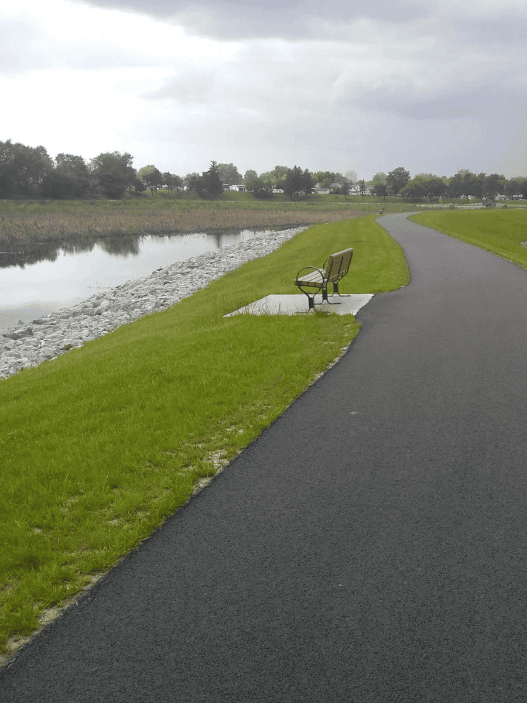 Serene lakeside walking trail with bench and scenic views, perfect for outdoor relaxation and nature exploration.