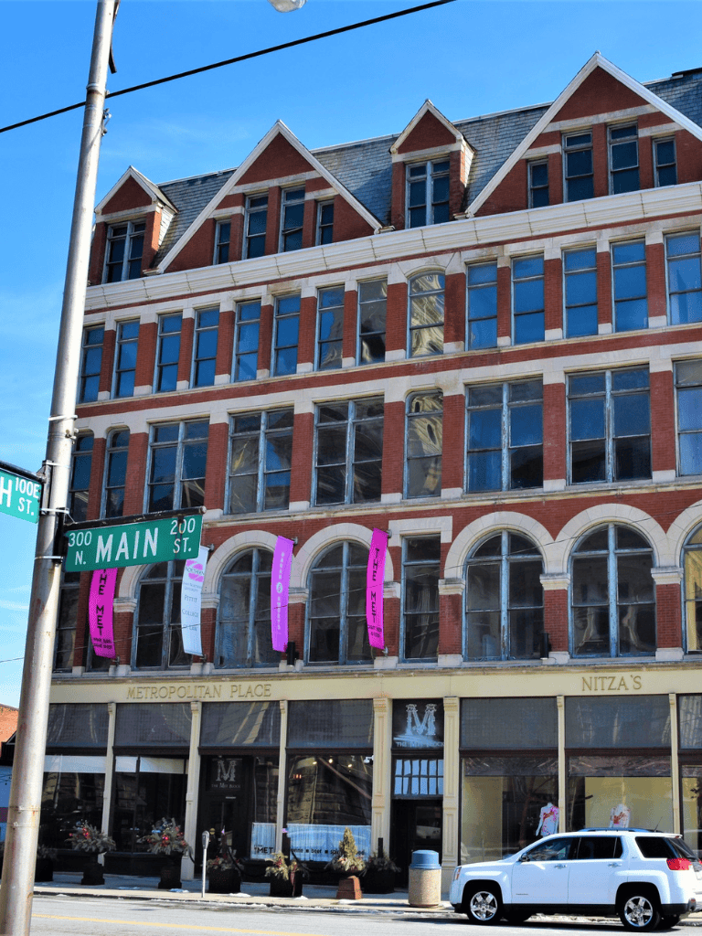 Downtown historic building with banners, parking, and street signs on Main Street in a city setting.