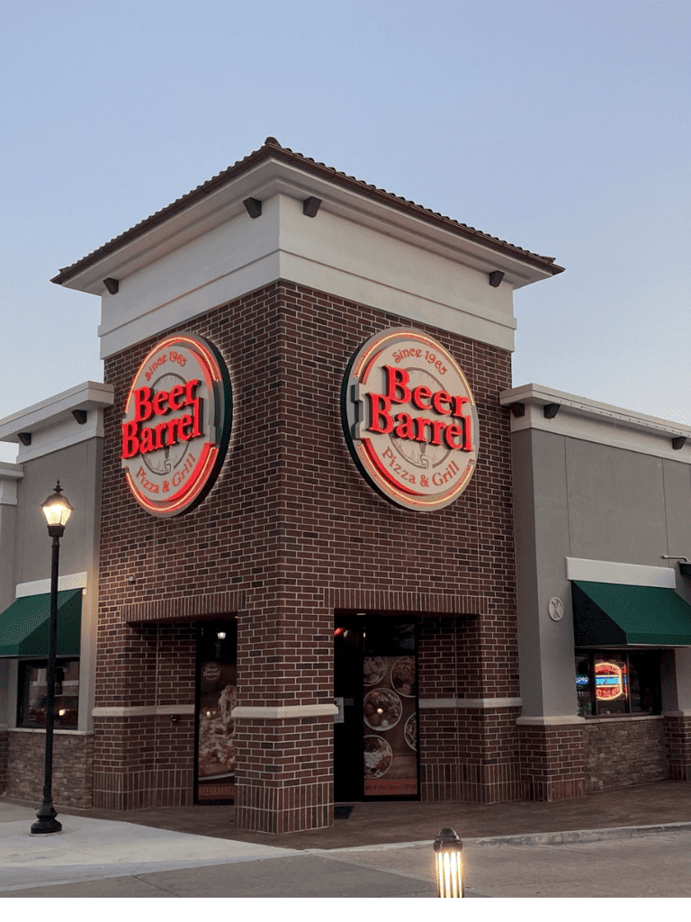 Beer Barrel pizza and grill restaurant exterior at dusk, featuring illuminated sign and brick facade.