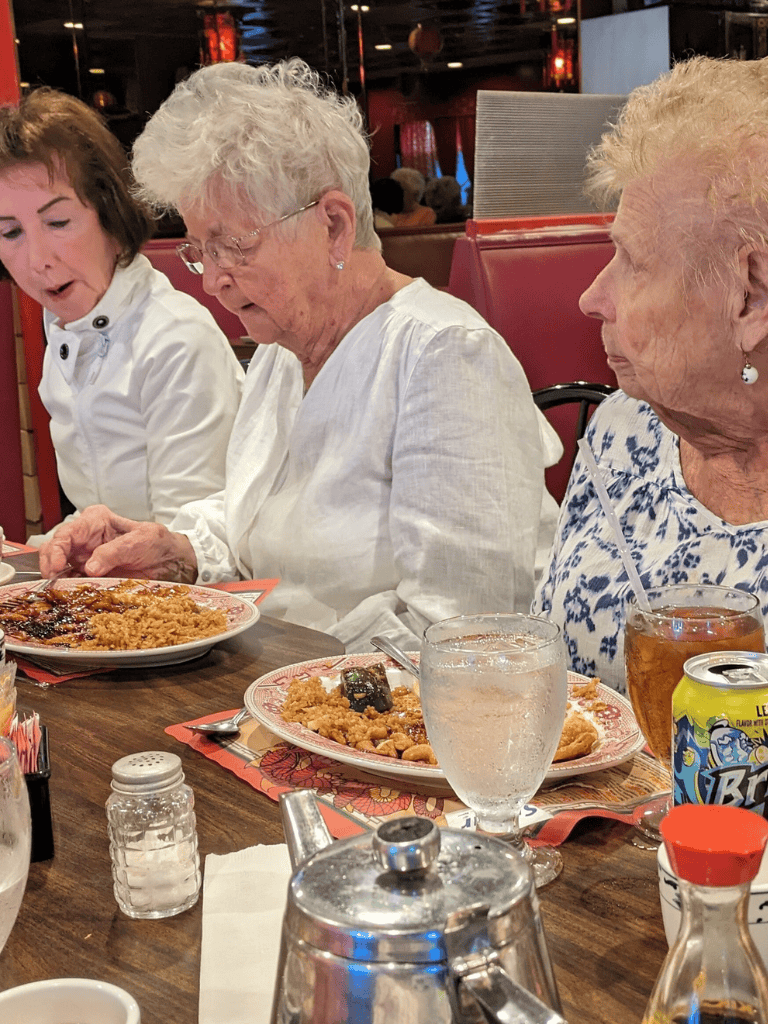 Delicious fried rice and sesame chicken at a cozy restaurant, enjoyed by elderly women with drinks.