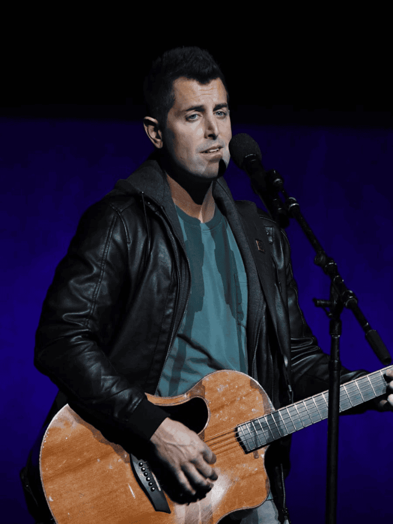 Performing musician with acoustic guitar on stage at QuestForDirections event.